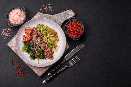 Warm salad consisting of slices of roast beef, greens, tomatoes, cucumbers, green beans on a dark concrete background