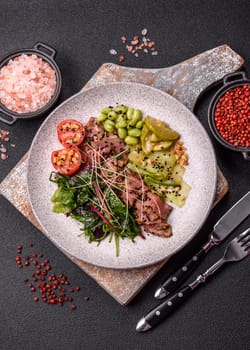 Warm salad consisting of slices of roast beef, greens, tomatoes, cucumbers, green beans on a dark concrete background