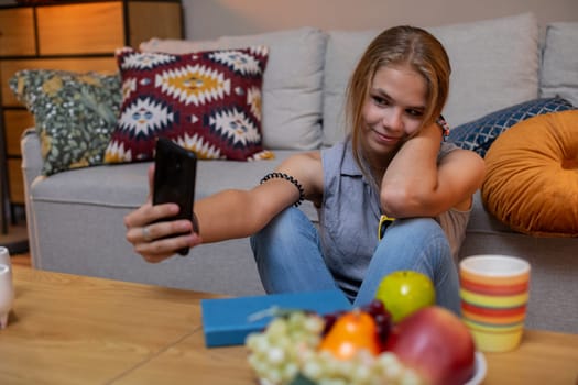 A young woman is capturing a vibrant selfie in a cozy living room filled with colorful fruits all around her