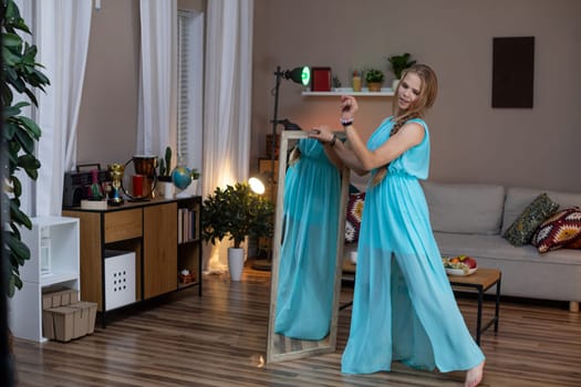 A stylish woman in an aqua dress confidently poses in front of a sleek mirror in a modern living room