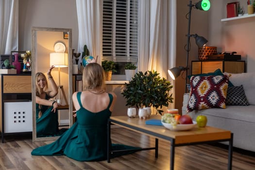 In a stylish and elegant room, a graceful woman wearing a beautiful green dress sits peacefully beside a mirror
