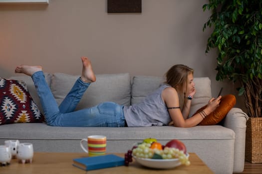 A person is blissfully relaxing on a cozy couch, happily enjoying their smartphone surrounded by delicious snacks