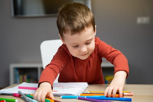 A cute happy little toddler boy of two years playing with markers in the album in the children's room at home. Educational activities for kids. Selective focus.