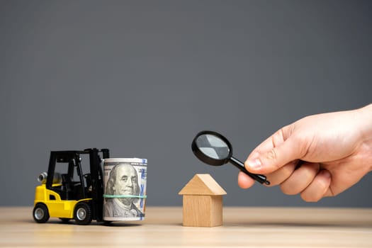 Real estate construction investment concept. Mortgage and finance. Buying and selling housing. Hand holding magnifying glass near house and forklift with money. Property refinancing