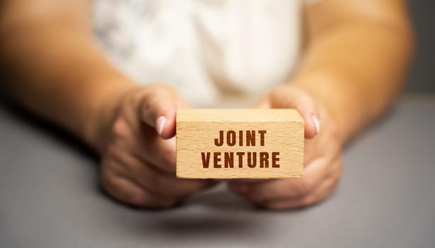 Joint venture on blocks concept. JV is a business entity created by two who parties shared returns and risks and shared governance. Wooden blocks in female hands