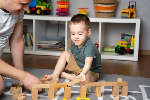 Little toddler boy 2,5 years playing wooden blocks with dad. Spending time with children. Educational activities for kids. Children's room. Indoors