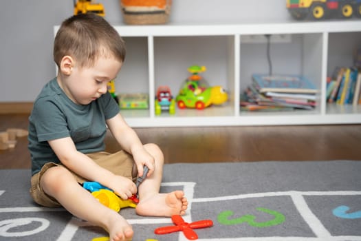 A little toddler boy 2.5 years is playing with a toy helicopter, assembling and disassembling it. Educational toys for kids. Children's room in home. Indoors