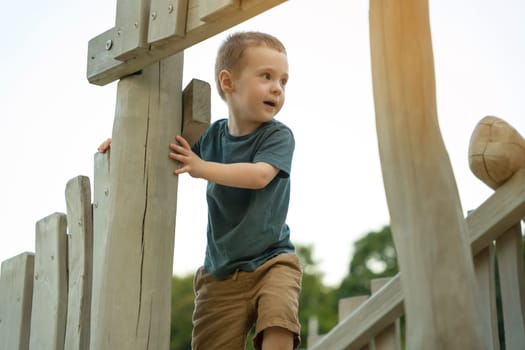 A cute curious toddler boy of two or three years playing on a wooden playground outside. Active games and entertainment for children. Summer day. Selective focus