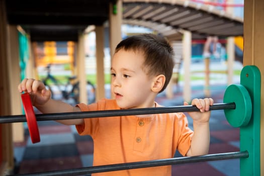 Cute toddler boy two or three years old is playing on the playground with wooden colorful rings on a sunny summer day. Children's games. Close-up. Selective focus