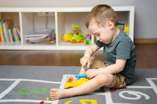 A little toddler boy is playing with a toy helicopter, assembling and disassembling it. Educational toys for kids. Children's room in home. Indoors