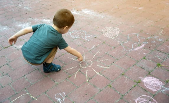 Little toddler boy two or three years old draws sun with crayons in the park on tiles. Playtime for children. Children's games. Selective focus