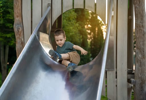 A cute toddler boy of two or three years going down the slide in the playground on a summer day. Active kid playing outside. Selective focus