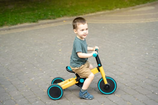 A cute toddler boy of two or three years old rides a bicycle or balance bike in a city park on a sunny summer day. Toddlerhood and childhood concept. Selective focus