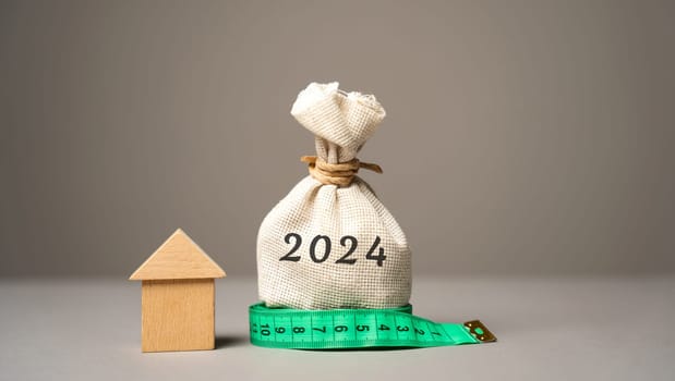 Wooden house and money bag 2024. Family budget planning for next year. Investments, plans, savings. Mortgage rates. Real estate concept. Refinance home.