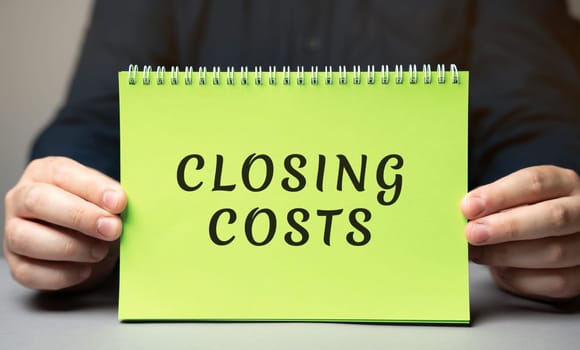 Closing costs concept. Extra amount of money that you pay when buying a house. Real estate and finance concept. Note in the hands of a businessman