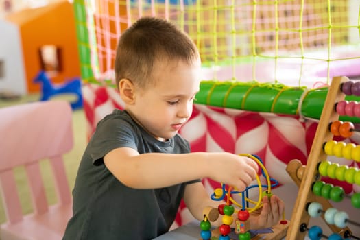 Toddler boy plays with educational wooden toy in children's playroom. Childhood concept. Selective focus