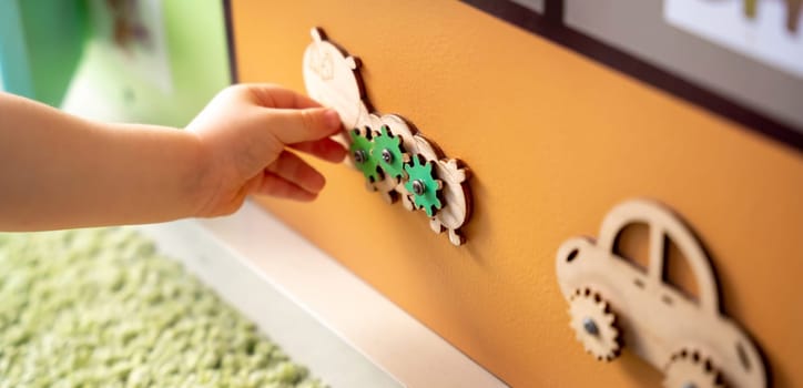 Toddler boy is playing with a busy board. Educational toy for young children. Focus on a wooden caterpillar. Close up