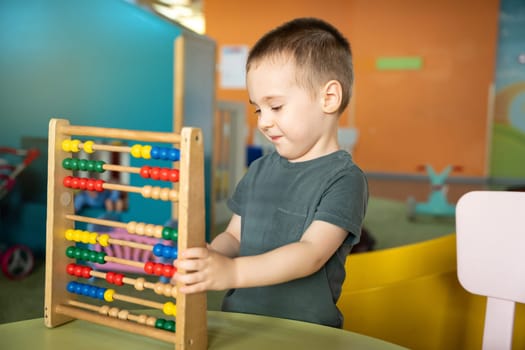 Smiling toddler boy playing with colourful toy abacus in a children's entertainment center. Educational toys for children. children's pastime