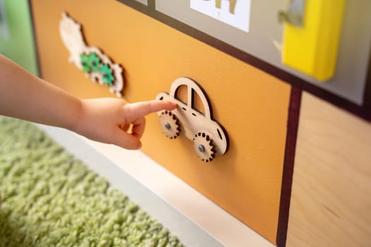 Toddler boy is playing with a busy board. Educational toy for young children. Focus on a wooden car. Close up