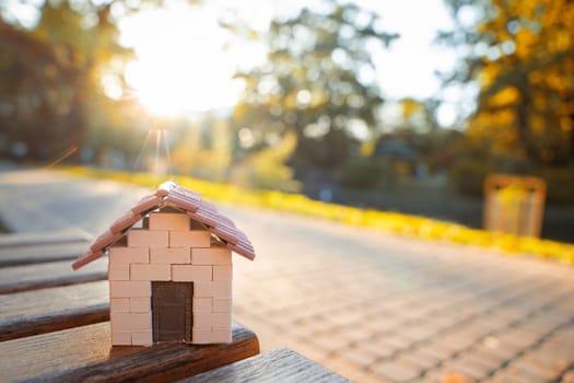 A miniature house stands on a bench in the park in the light of the setting sun. Real estate, affordable housing and mortgage lending concept. Sale, purchase and rental of apartments. Selective focus