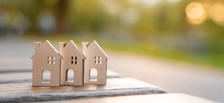 Three wooden miniature houses stand on a bench in the park on a sunny day. Real estate and affordable eco-friendly housing concept. Mortgage, loan and insurance of apartments. Selling and buying home