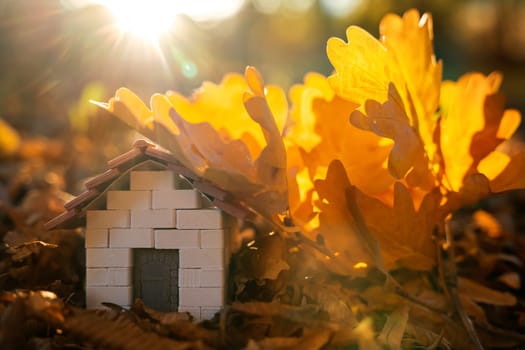 Miniature wooden house with yellow leaves on a sunny autumn day. Real estate and affordable housing concept. Mortgage, loan and insurance of apartments. Selling and buying home. Sunset