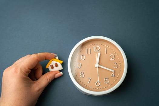 A miniature house in hands and a clock. Mortgage and loan concept. Temporary rental housing and residence permit. Real estate. Time to pay taxes and bills. Restriction of stay, reservation.