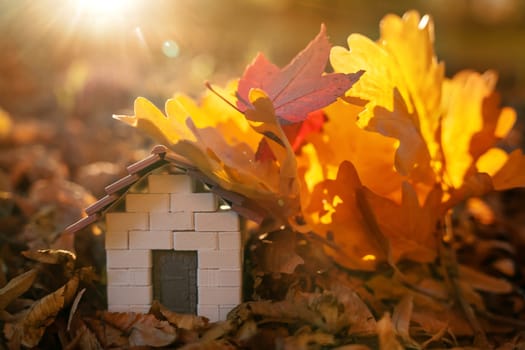 Miniature wooden house with yellow leaves on a sunny autumn day. Real estate and affordable housing concept. Mortgage, loan and insurance of apartments. Selling and buying home. Sunset