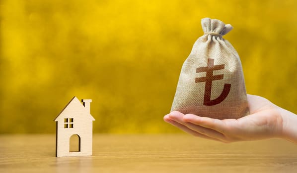 Turkish lira money bag and miniature wooden house on a yellow background. Real estate and affordable housing concept. Mortgage, loan and insurance of apartments. Selling and buying home.