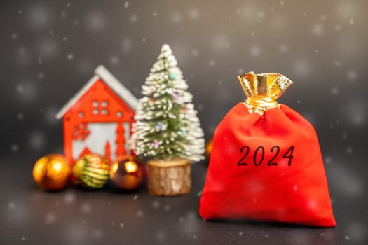 Red gift bag 2024, Christmas tree and miniature house. Merry Christmas and Happy New Year! Xmas concept. Festive winter holiday. Snowfall