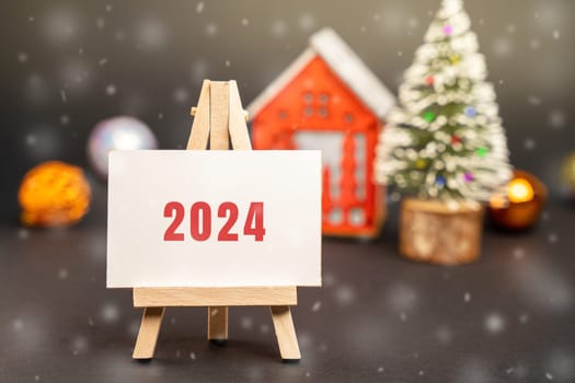 Easel 2024 with house and Christmas tree. Happy New Year or Xmas winter holiday. Decoration, celebration. The concept of the beginning of the new year. Snow, snowfall