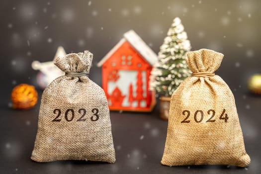 Bags 2023, 2024 in the background of a New Year tree, a house and snow. Concept of financial savings and money management. Profit analysis and budget planning for the new year. Business and finance
