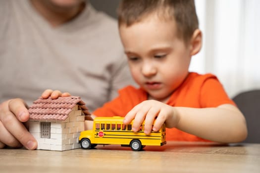 Dad and son play with a house and a school bus. Spending time with children. The concept of a happy childhood. Indoor, home