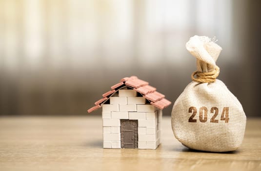 Money bag 2024 and miniature house. Family budget planning for next year. Mortgage rates and credit. Real estate fund concept. Refinance home.
