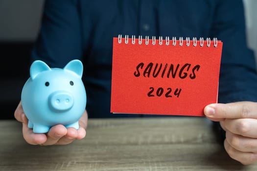 Savings 2024 concept. Accumulating money for the New Year. Budget and expense planning. A notepad in the hand of a businessman and a piggy bank. Business and finance