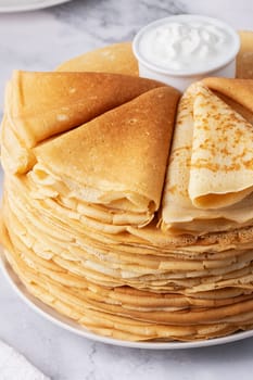 Stack of traditional russian pancakes blini with sour cream on marble background.