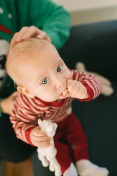 An adorable baby sits calmly, sucking their tiny thumb while holding a soft toy, showcasing pure innocence