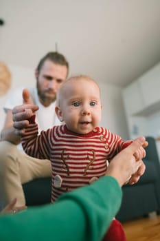 A joyful moment occurs as a baby practices walking with attentive, loving parents in a cozy living space