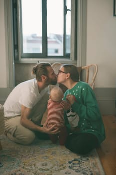 In a tender moment, a loving couple shares a kiss while gently holding their precious baby in a cozy home setting