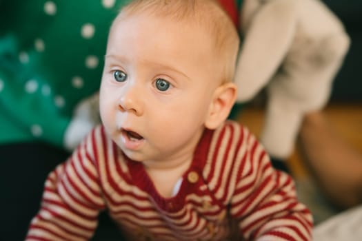 A closeup of a curious baby with blue eyes, dressed in colorful stripes, surrounded by warmth and joy