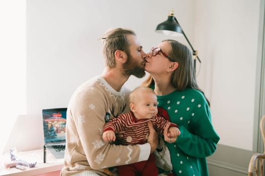 A heartwarming family moment showcasing loving parents kissing their sweet little baby dressed in festive outfits