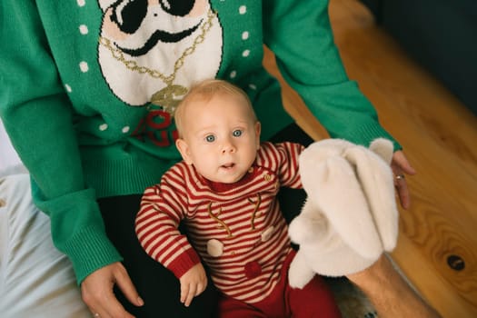 A delightful cute baby dressed in a festive attire, comfortably seated with a soft plush toy, spreading holiday cheer