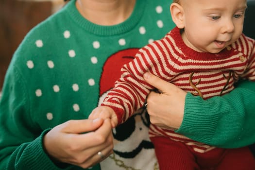A woman joyfully holds a baby in matching holiday sweaters, celebrating the festive season with love