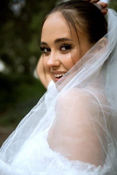 close-up of a bride with a white veil. beautiful brunette girl with a smooth hairstyle and stylish makeup. near her face is a white elegant veil. the girl is smiling
