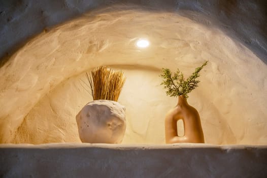 decorative handmade clay pottery in an arch with lighting. in craft products green cypress branches and yellow ears of corn. close-up of natural dishes, environmentally friendly