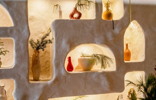decorative wall with backlight and arches in which stand handmade vases. beige wall in it stand vases with flowers. arches are illuminated with warm light. photo horizontal orientation