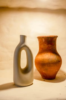 decorative handmade clay pottery on a shelf with lighting. close-up of natural pottery, eco-friendly, two items stand next to each other, this is a jug and a vase hard light
