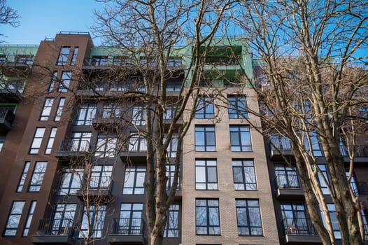 A tall building. High quality photo, multi-storey new house with energy-saving facade. brown wall with light stripes in front of the house autumn trees. the house has 5-6 floors