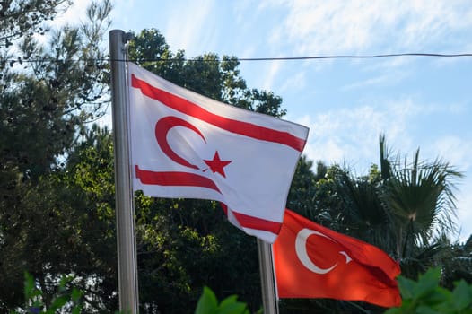 Flags proudly display their colors and symbols on a clear day, surrounded by green trees and vibrant plants.