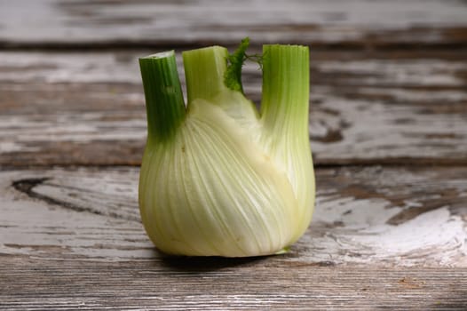 A vibrant fennel bulb stands upright on a weathered wooden surface, showcasing its fresh green tops and smooth texture.